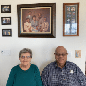 Kathy and John Harris sitting under wall hung family photos.