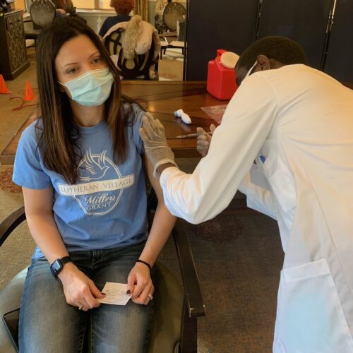 Executive Director, Michelle Rosenheim, sitting in a chair about to get injected with the COVID-19 vaccination.