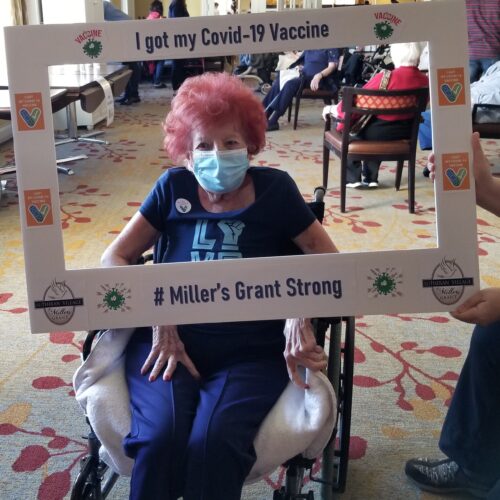A Health Care Center resident of LVMG sitting in her wheel chair with someone holding an I Got My COVID-19 Vaccine selfie frame in front of her.
