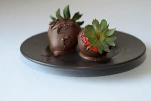 Two dark chocolate covered strawberries on a plate.