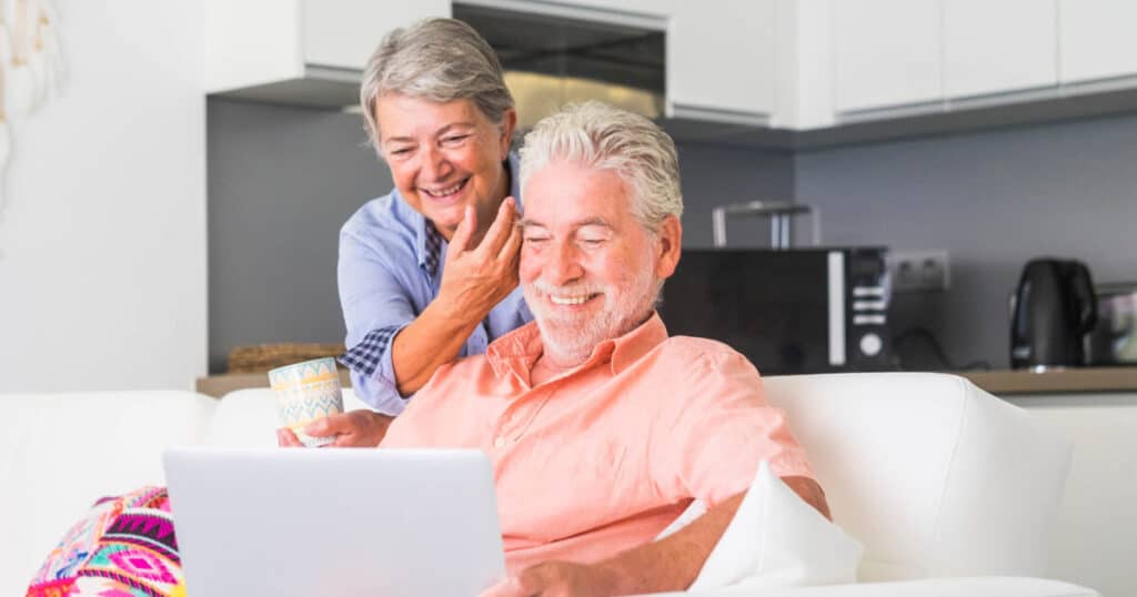 An older adult couple researching CCRC senior living amenities and services on a laptop computer.
