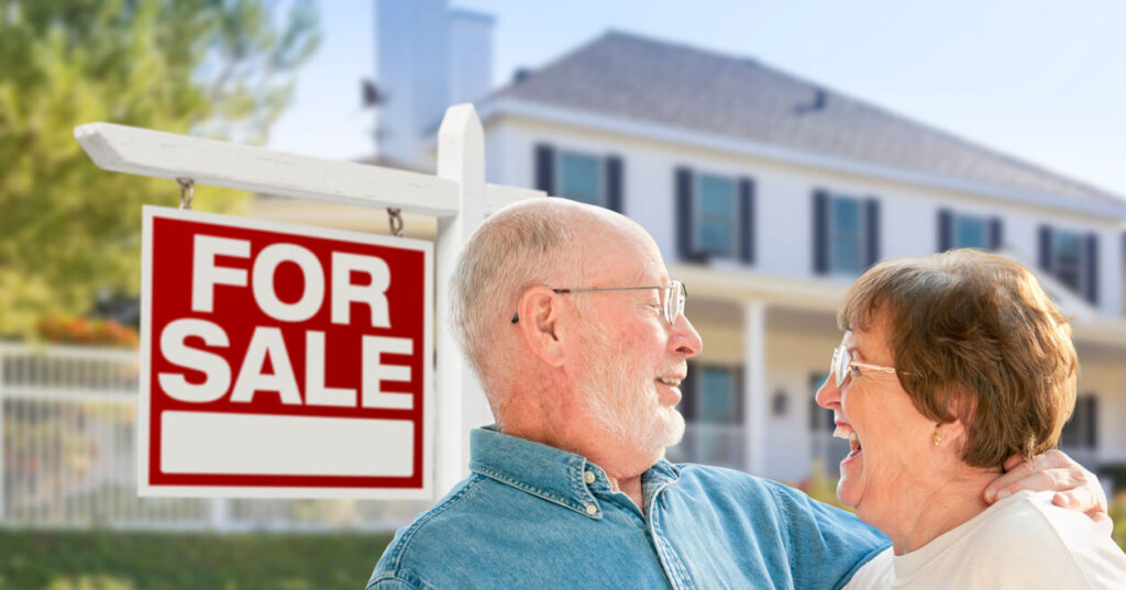 A happy senior couple standing in front of a for sale sign after they worked to prepare their home for sale.