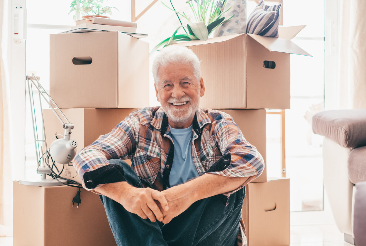 A senior man sitting in front of boxes looking happy to be moving to an active adult retirement living community.